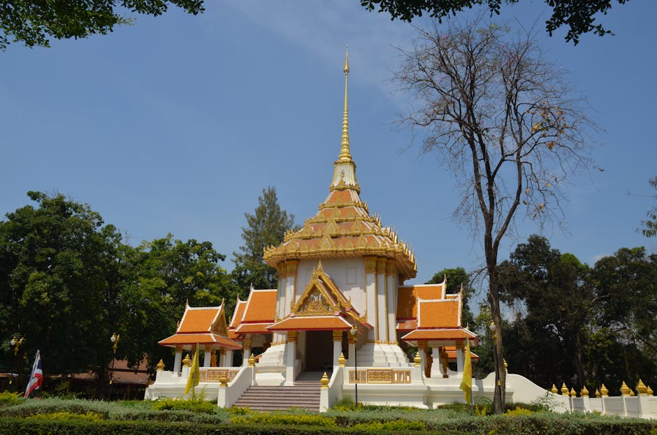 Ornate Thai temple with golden details surrounded by trees under a clear sky.